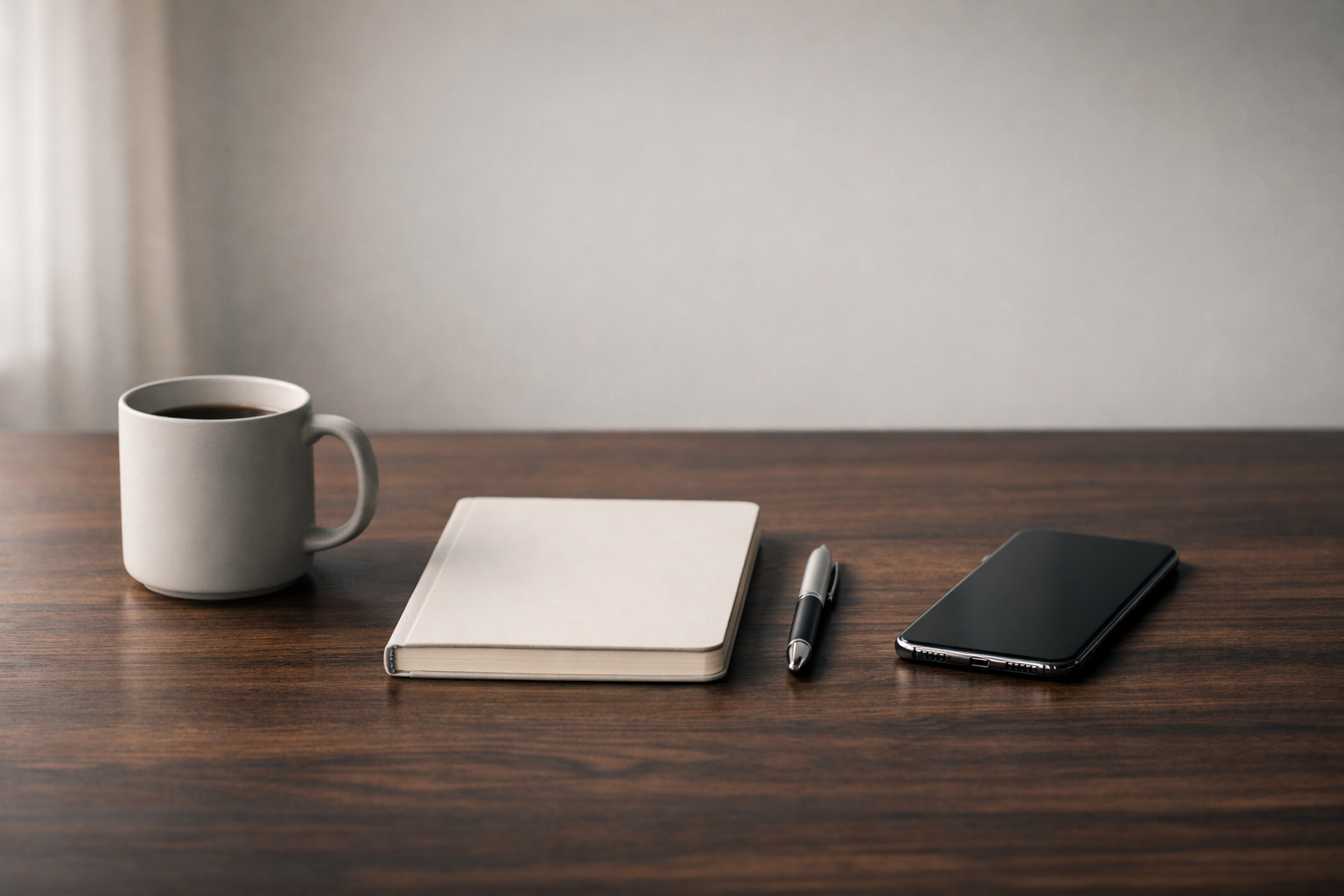 Minimalist professional desk setup with notebook, pen, phone, and coffee mug in soft natural light